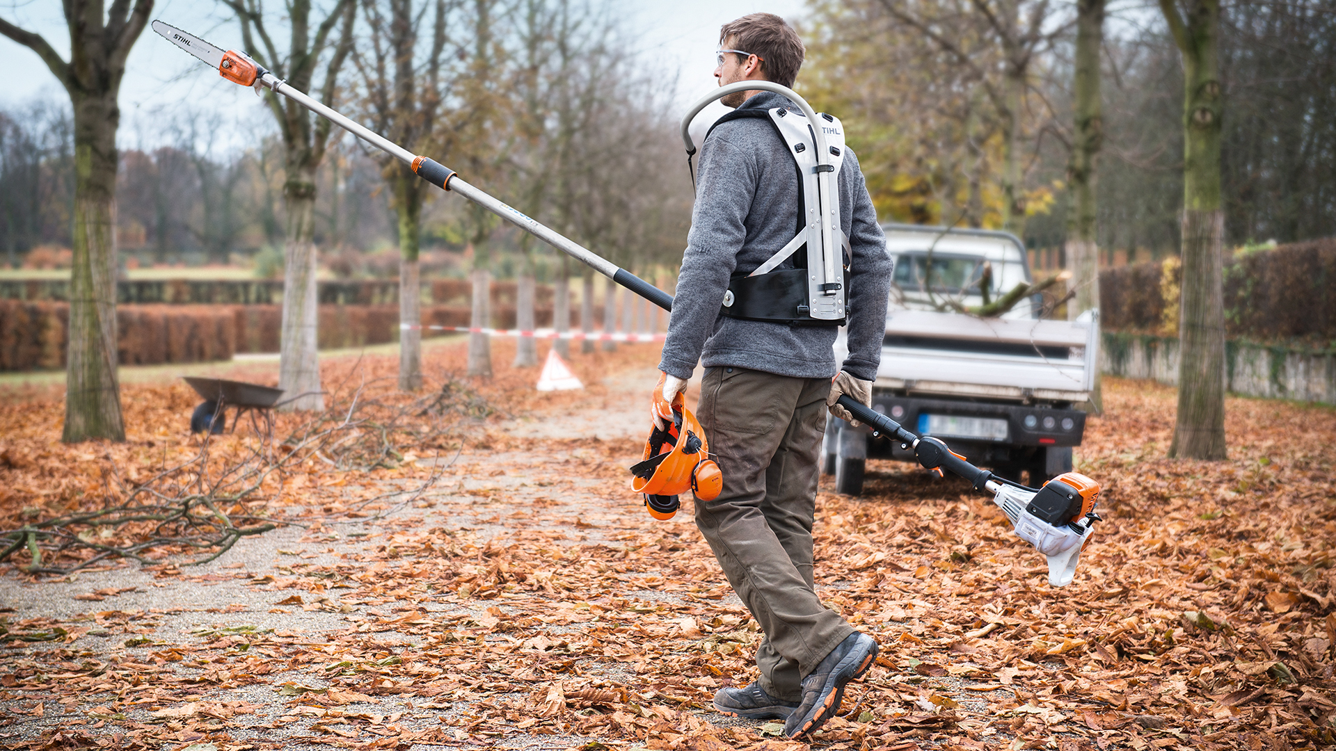 Mies STIHL HT 133 -bensiinileikkurilla ja työajoneuvolla puistossa syksyllä