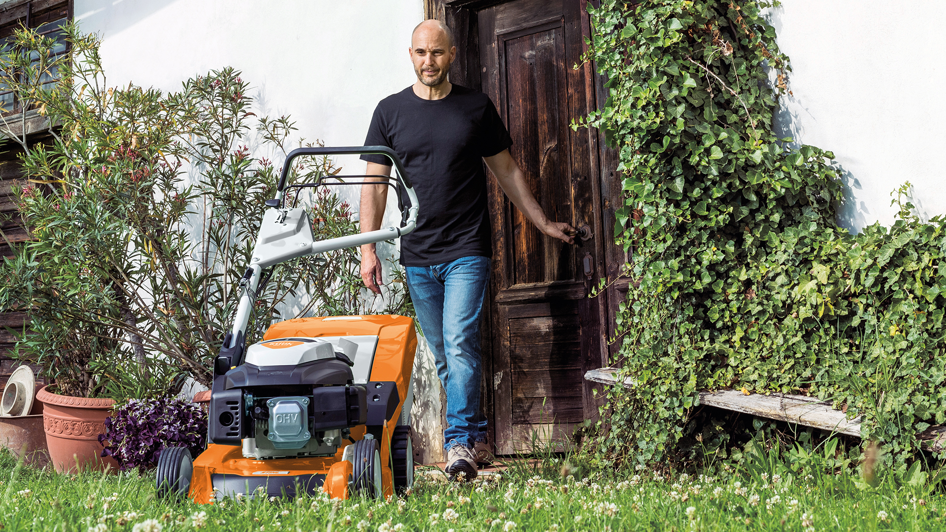 Mies kävelee ovesta puutarhaan STIHL RM 650 -bensiiniruohonleikkurille