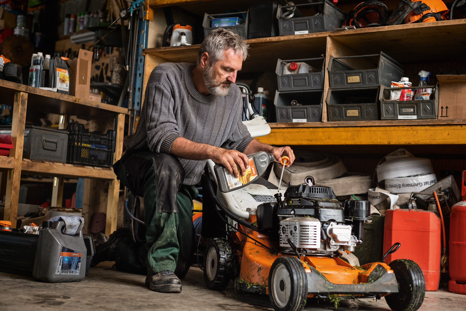 Mies huoltamassa STIHL RM 756 -bensiinikäyttöistä ruohonleikkuria autotallissa