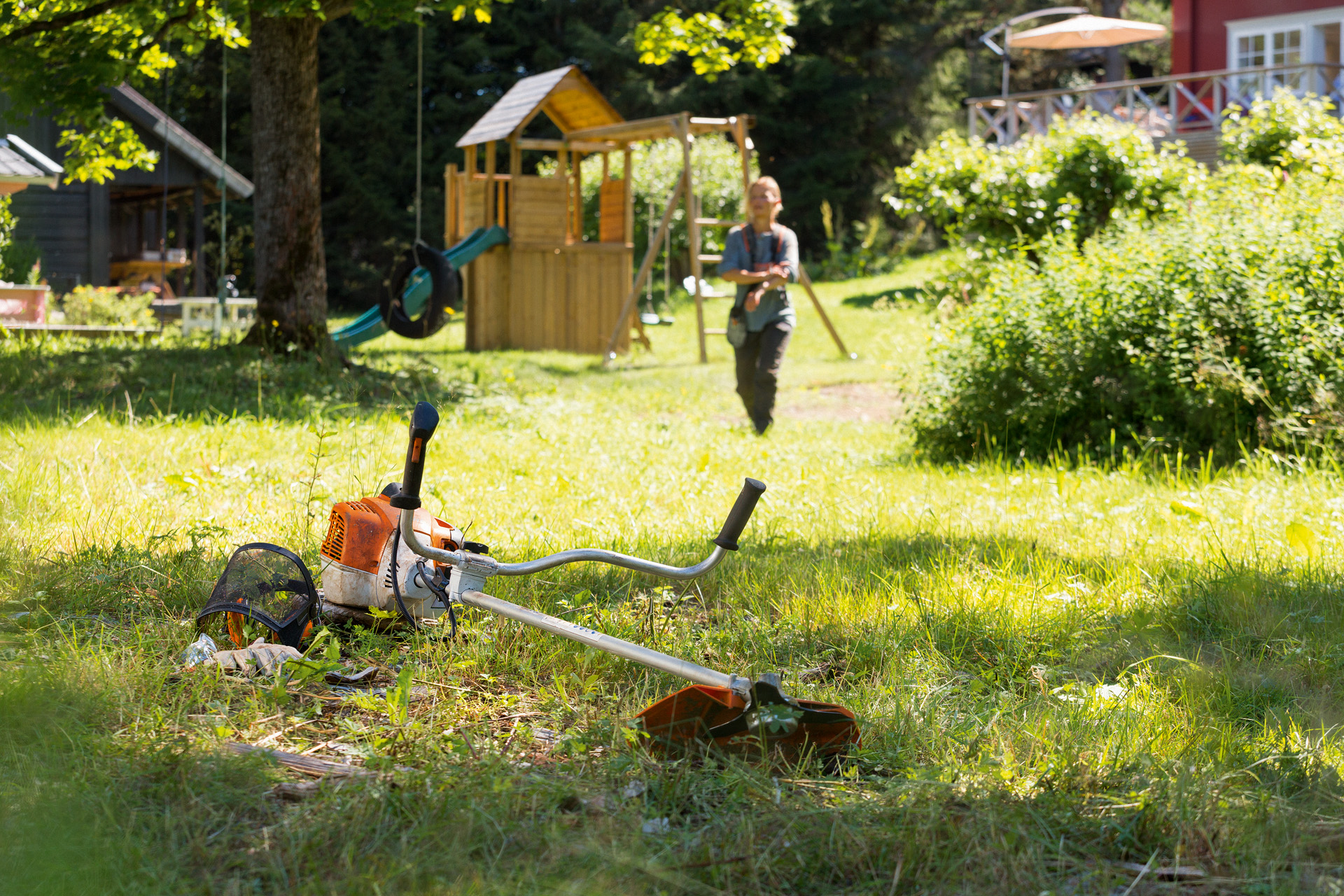 STIHL FS 240 -raivaussaha ruoholla, taustalla kunnossapitoon valmistautuva mies