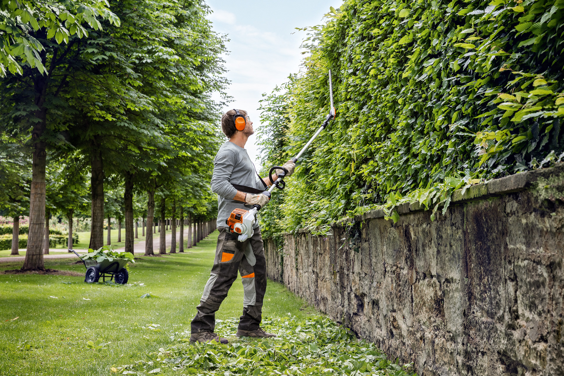 Suojavaatteisiin pukeutunut mies leikkaa pensasaidan sivua pystysuunnassa STIHL pensasleikkurilla HL 94