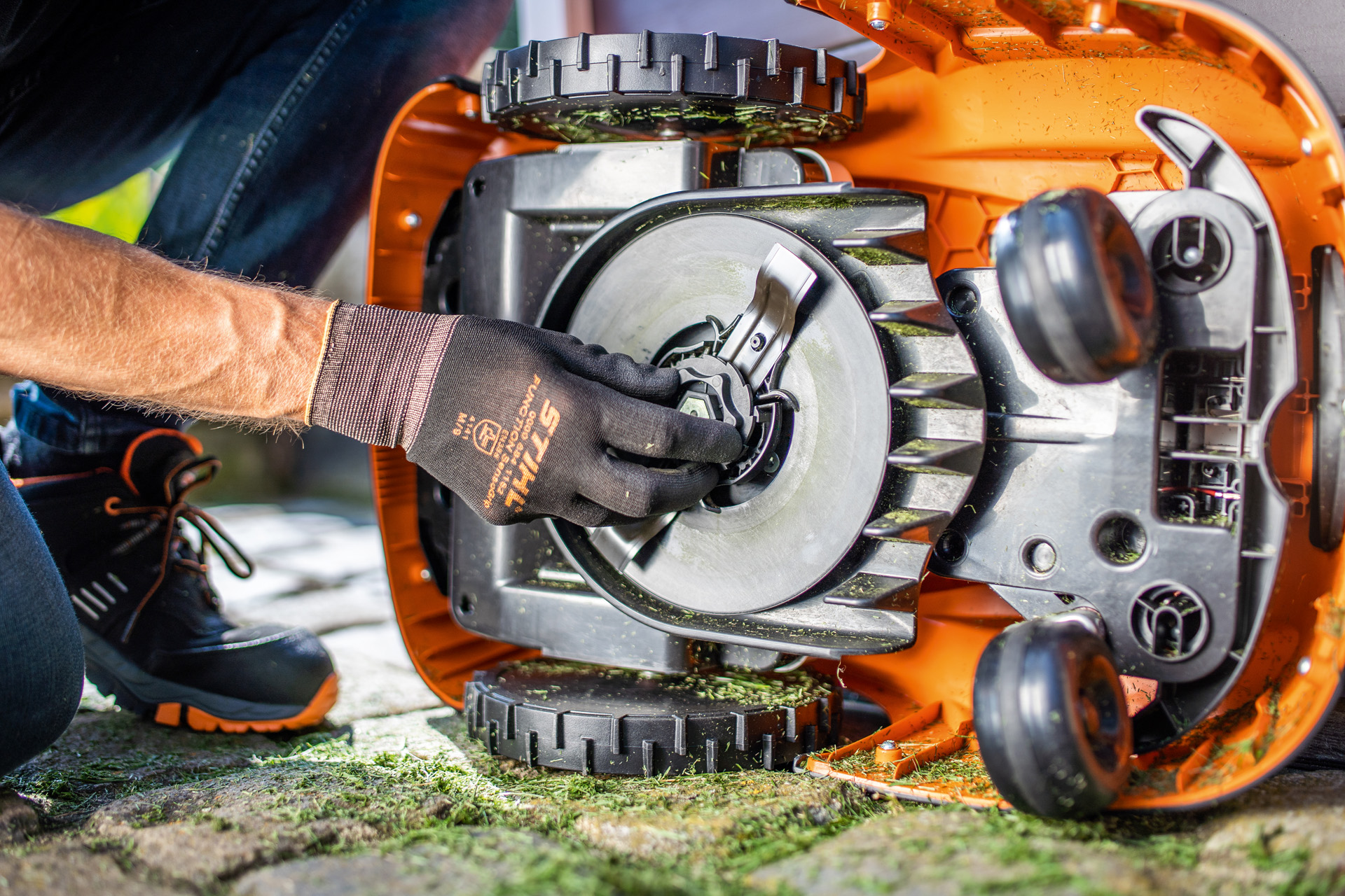 Näkymä STIHL iMOW® -robottiruohonleikkurin puhtaasta alaosasta, kun sitä tarkistetaan käsineet kädessä