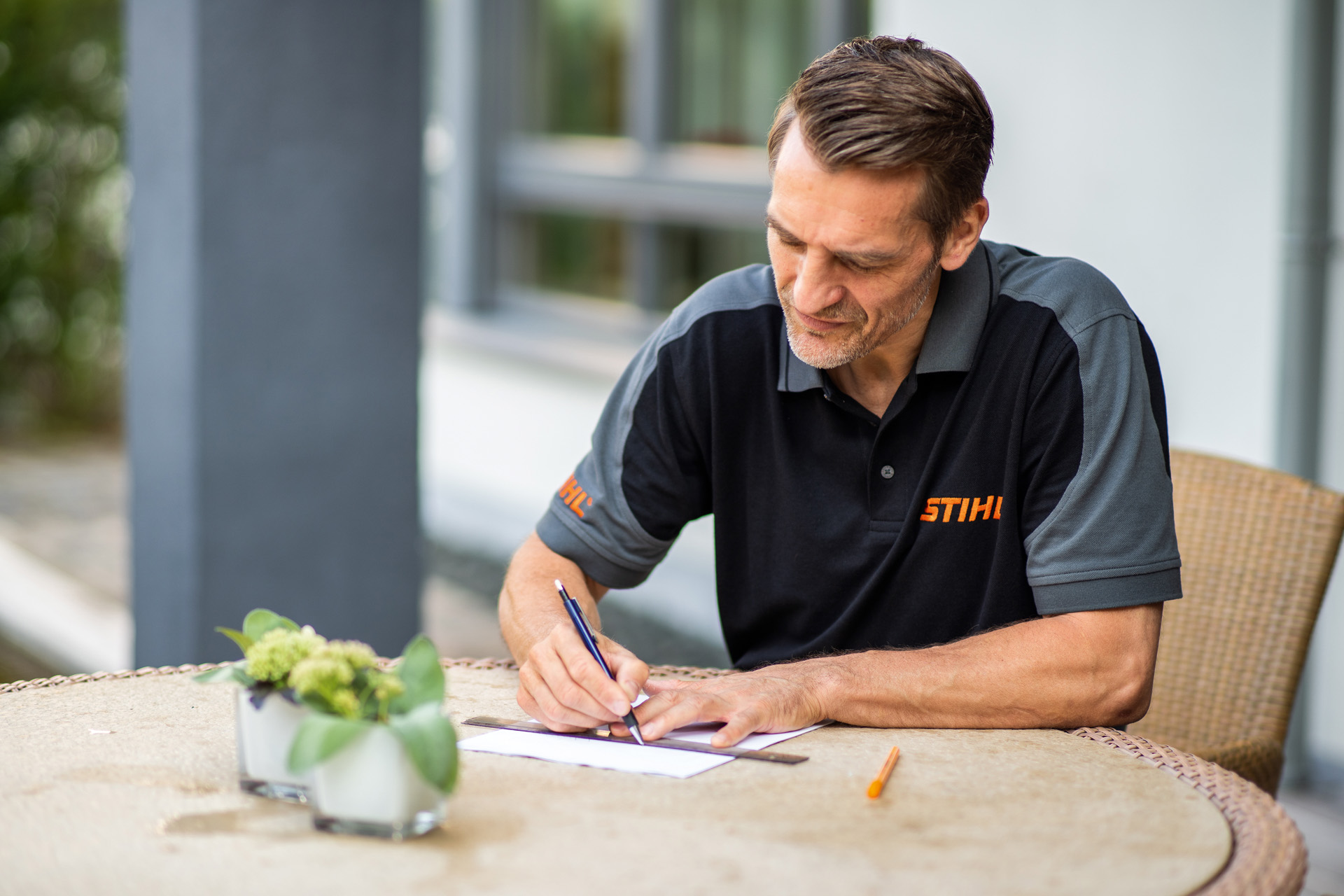 STIHL-jälleenmyyjä istumassa puutarhapöydän ääressä ja laatimassa suunnitelmaa iMOW-robottiruohonleikkurilla leikattavasta nurmikkoalueesta
