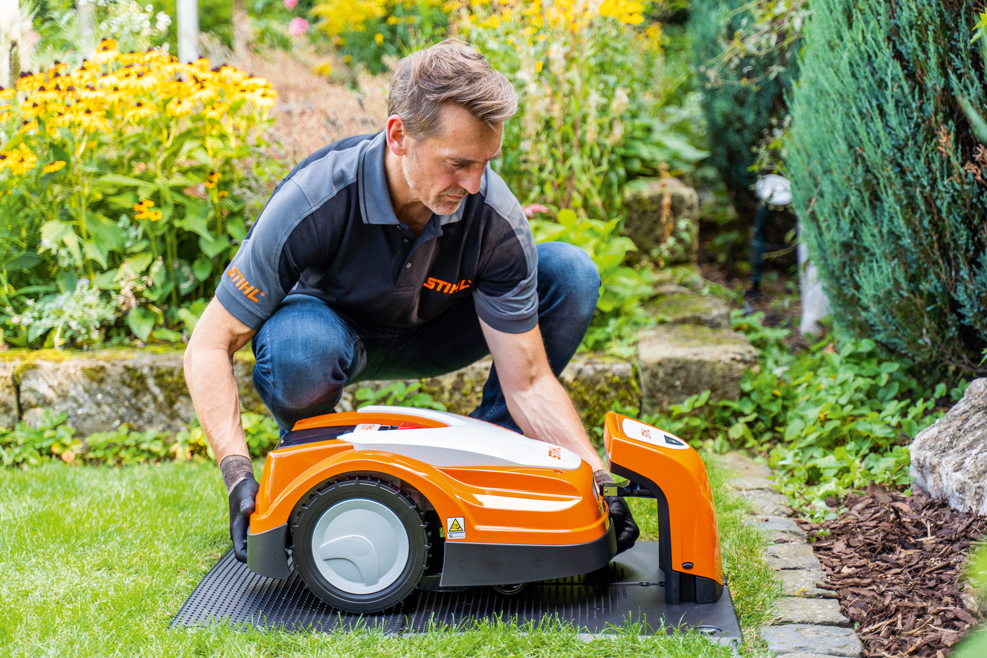 STIHL-jälleenmyyjä asettaa STIHL iMOW -robottiruohonleikkurin latausasemaansa puutarhaan