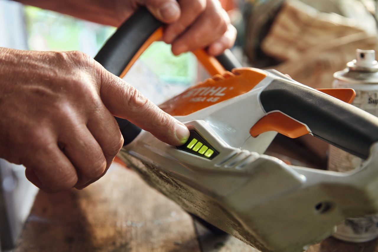 Henkilö tarkistaa STIHL HSA 45 -akkupensasleikkurin lataustason.