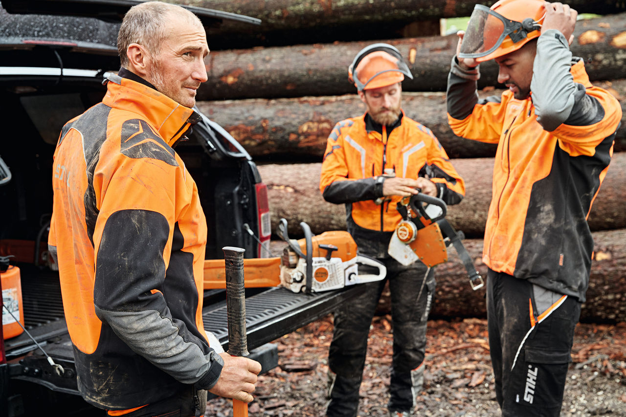 Kolme suojavarusteita käyttävää miestä ajoneuvon edessä ja avattu STIHL-akkutyökaluja sisältävä tavaratila