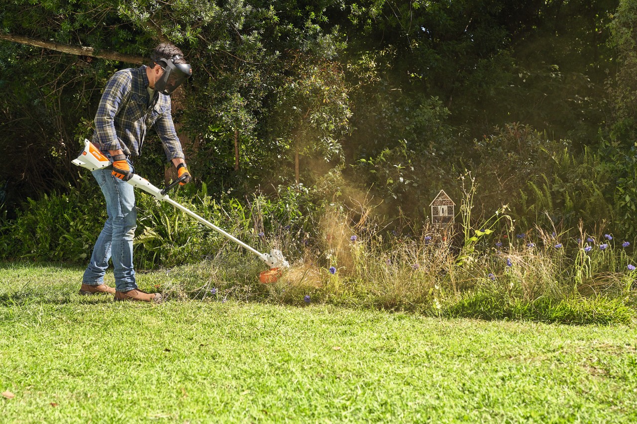 En man trimmar en äng med vildväxande blommor med en STIHL FSA 57