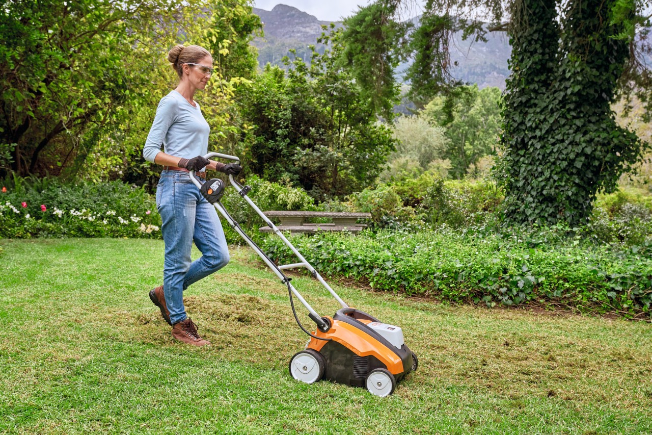 Frau mit Schutzbrille und Arbeitsschutzhandschuhen mäht mit einem STIHL Rasenmäher eine Wiese